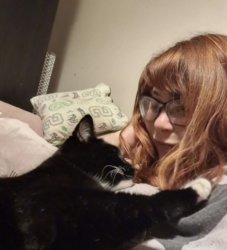 woman with long brunette hair and glasses with black-and-white cat lying on her chest