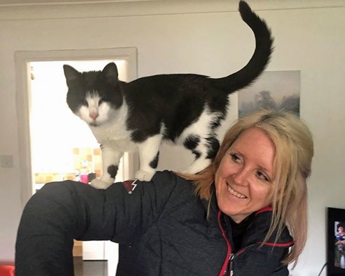 woman with long blonde hair with black-and-white kitten with no eyes standing on her shoulder