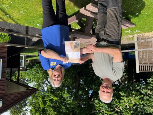 man with grey hair wearing grey t-shirt being handed certificate by blonde woman wearing Cats Protection blue t-shirt