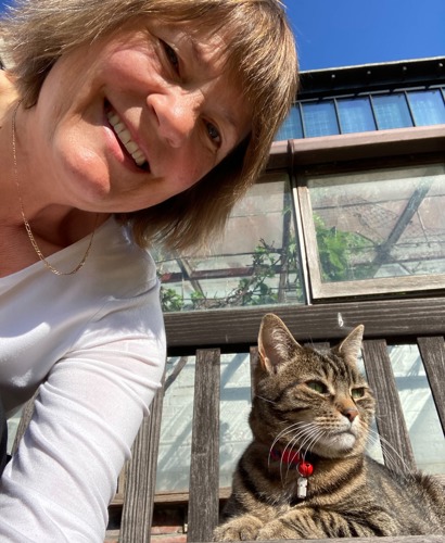 woman with short brown hair next to brown tabby cat sitting on a wooden bench