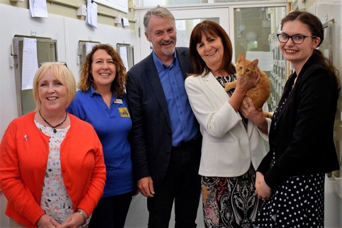 Four woman and one man stand in adoption centre corridor. One woman is holding a ginger cat