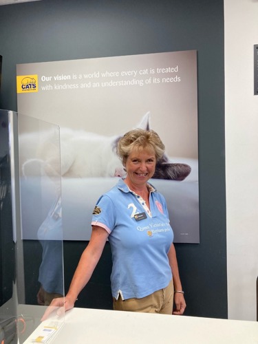 Woman with short blonde hair and blue tshirt standing behind shop counter