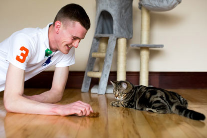 young man playing with tabby cat and toy mouse