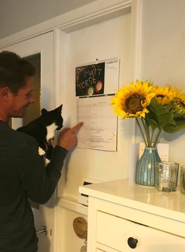 man holding black and white kitten pointing at calendar