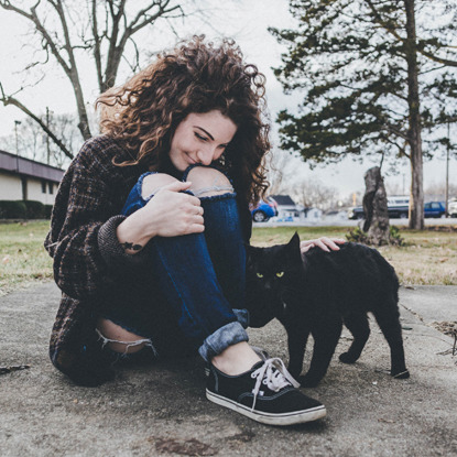 girl sitting on floor and stroking black cat