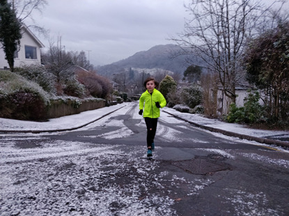 young boy in yellow jacket running along snowy road