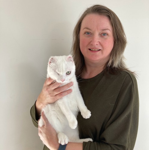 long-haired brunette woman holding white cat with one eye and ear tips missing