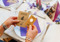 A person sitting at a dining table holding Cats Protection wedding favours: one packet of flower seeds and one pin badge